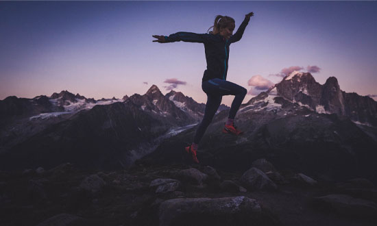 Jënni Jalonen gör ett skutt på löparrundan på en klippa. I bakgrunden syns berg och solnedgång