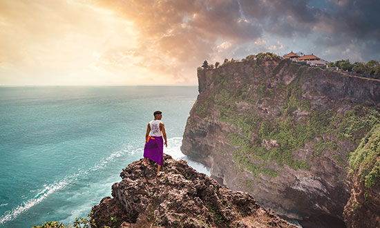 Balinesisk man som står på en klippavsats och ser ut över havet i Bali.