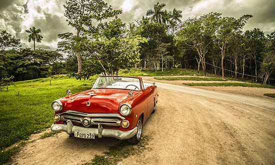 Röd bil i cab-modell står på en grusväg med växtlighet bakom