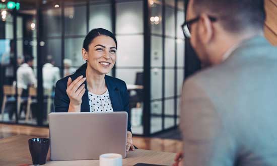 En kvinna som sitter på affärsmöte i kontorsmiljö. Man ser också ryggen på en man som hon är i möte med