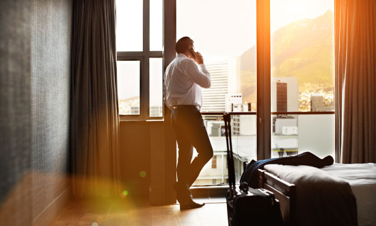 Affärsman på hotellrum som pratar i telefon. I förgrunden syns en säng och en resväska
