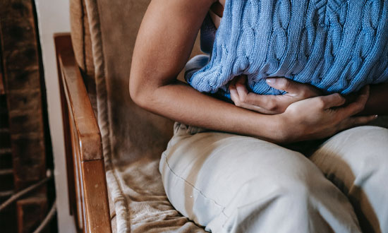 Kvinna i blå topp som håller sig för magen på grund av illamående