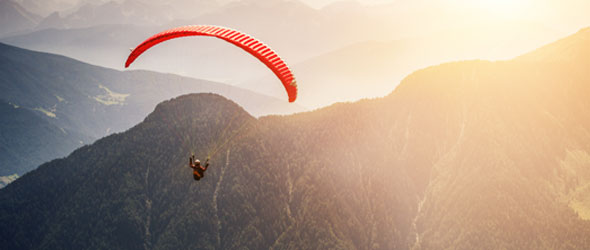 Person som gör paragliding i bergsmiljö. Solnedgången syns i bakgrunden. 