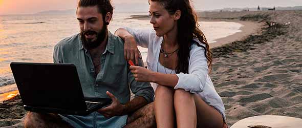 Digitala nomader som sitter på en strand och arbetar tillsammans på en laptop