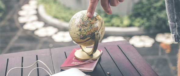 Ett bord med ett pass och en liten jordglob är ställd på passet. En person har satt sitt pekfinger på en destination på jordgloben