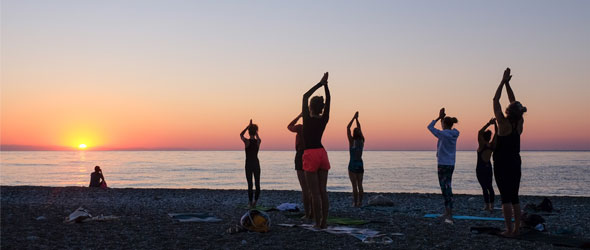 Människor på träningsresa som gör yoga på stranden i soluppgången. 