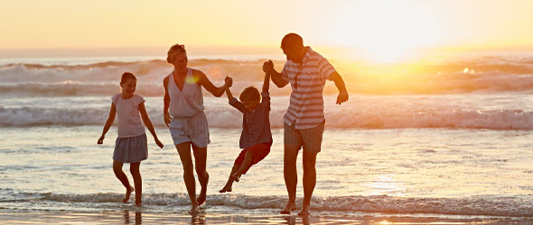 Mamma, pappa och två barn som är på stranden i solnedgång. Havet syns bakom dem. 