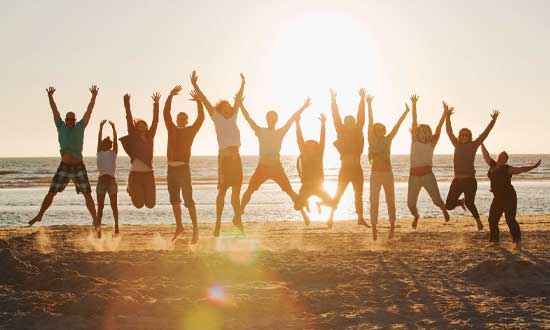 12 personer som gör glädjeskutt tillsammans på en strand i solnedgång.