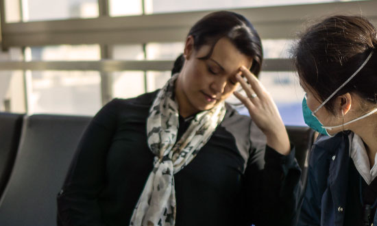 Kvinna som sitter på flygplats och mår dåligt. Jämte sitter en kvinnlig läkare.