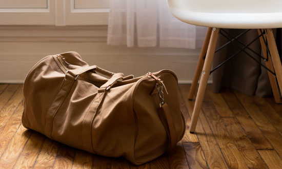 En mjuk resväska i brunt läder som står på golvet bredvid en stol.