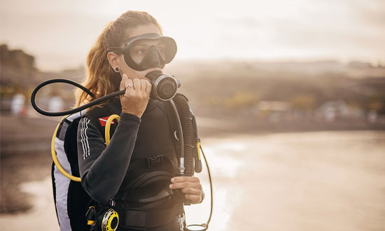 Kvinna med dykarutrustning. I bakgrunden syns havet.